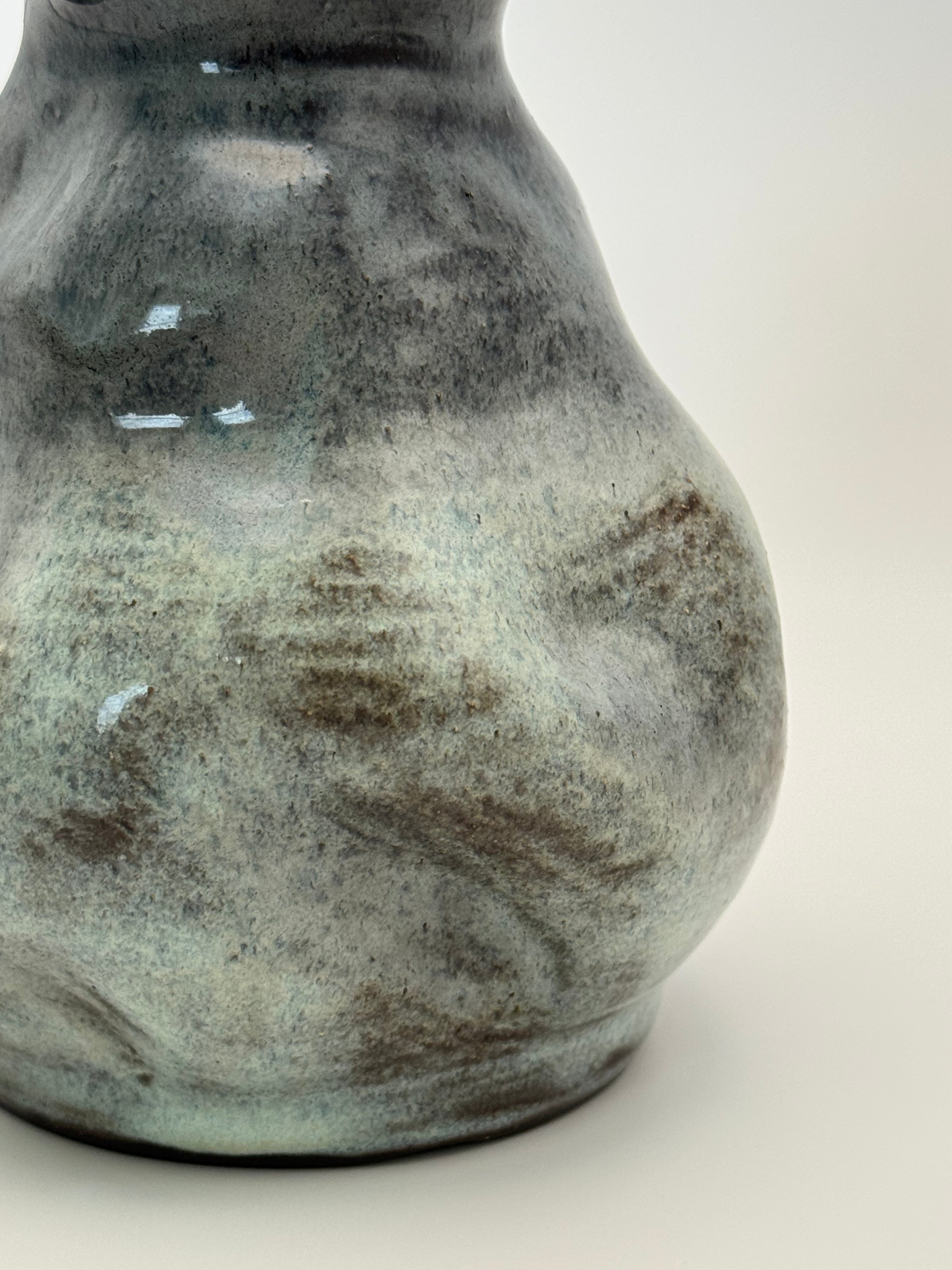 Close-up of a ceramic vase with a rounded body with soe dark brown clay showing through the glaze.