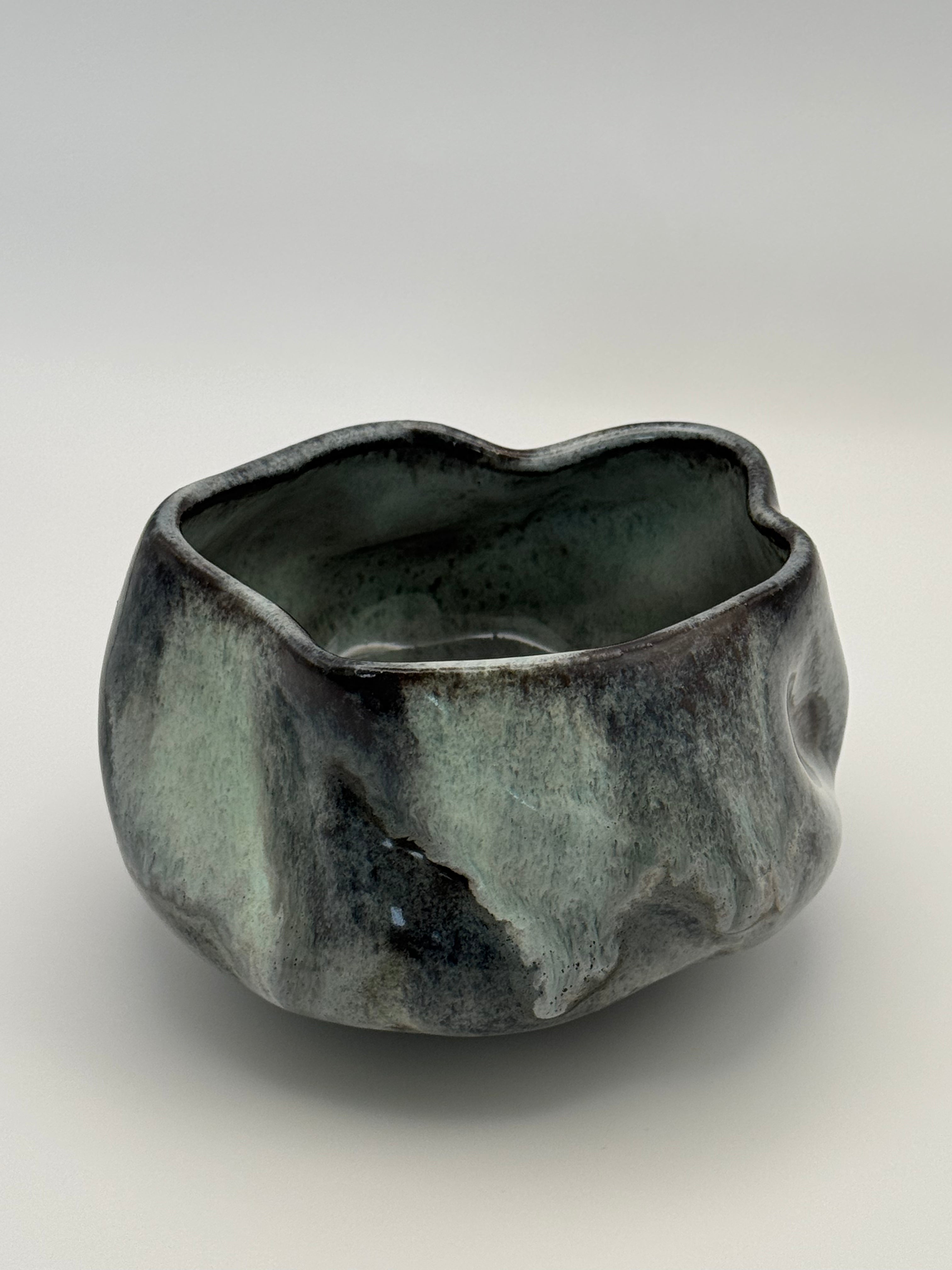 A rustic, organic-shaped ceramic bowl with a dark blue and light blue glaze, photographed on a neutral light gray background.