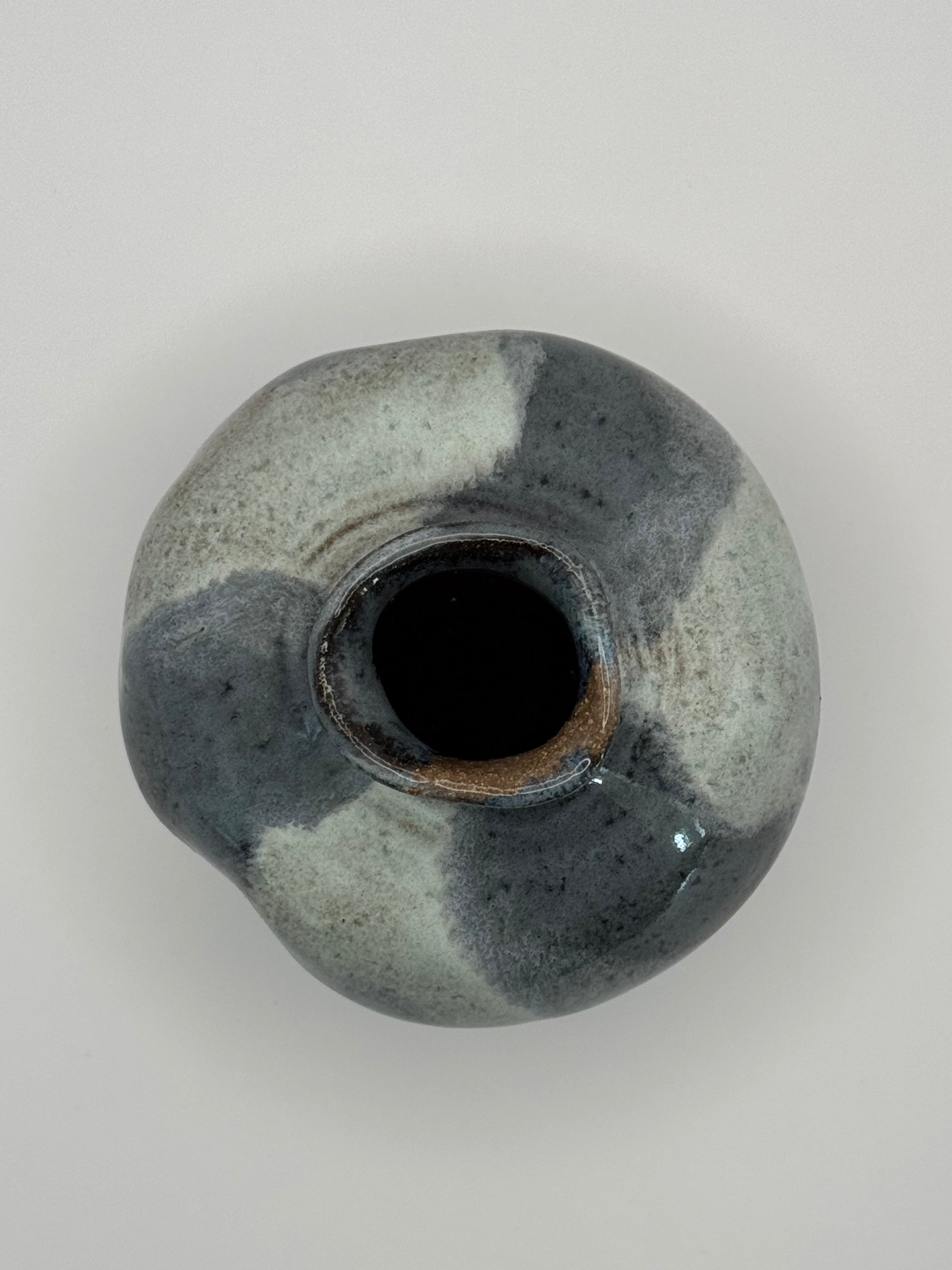 Top view of a handmade ceramic vase with a rounded bulbous body and a small flared rim, featuring a mottled glaze in shades of slate blue and blue-gray on a light neutral background.