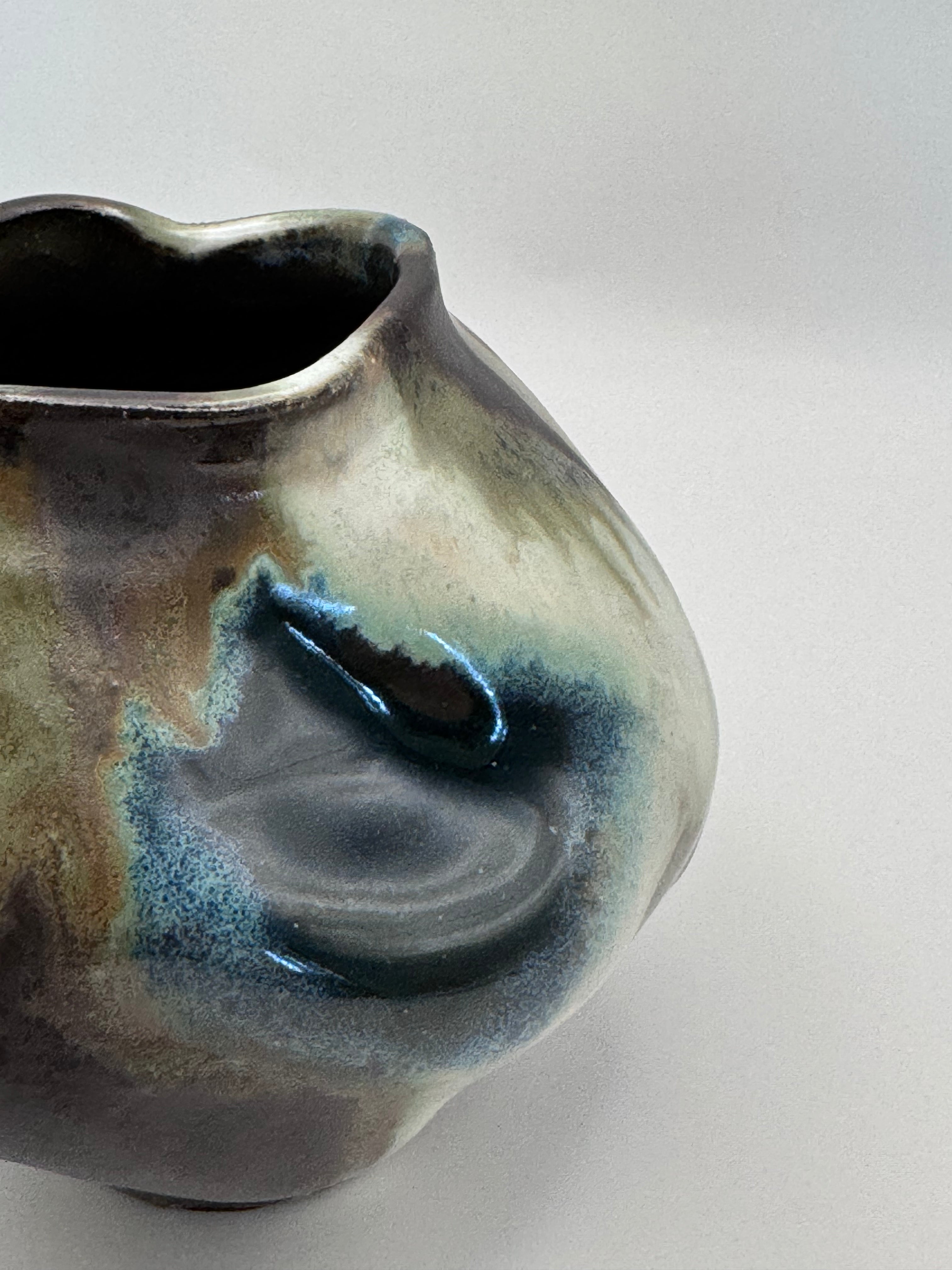 Side view of Hand-shaped ceramic vase with softly undulating walls and a wide mouth, marbled dark brown, white, green celadon, and light blue glaze.