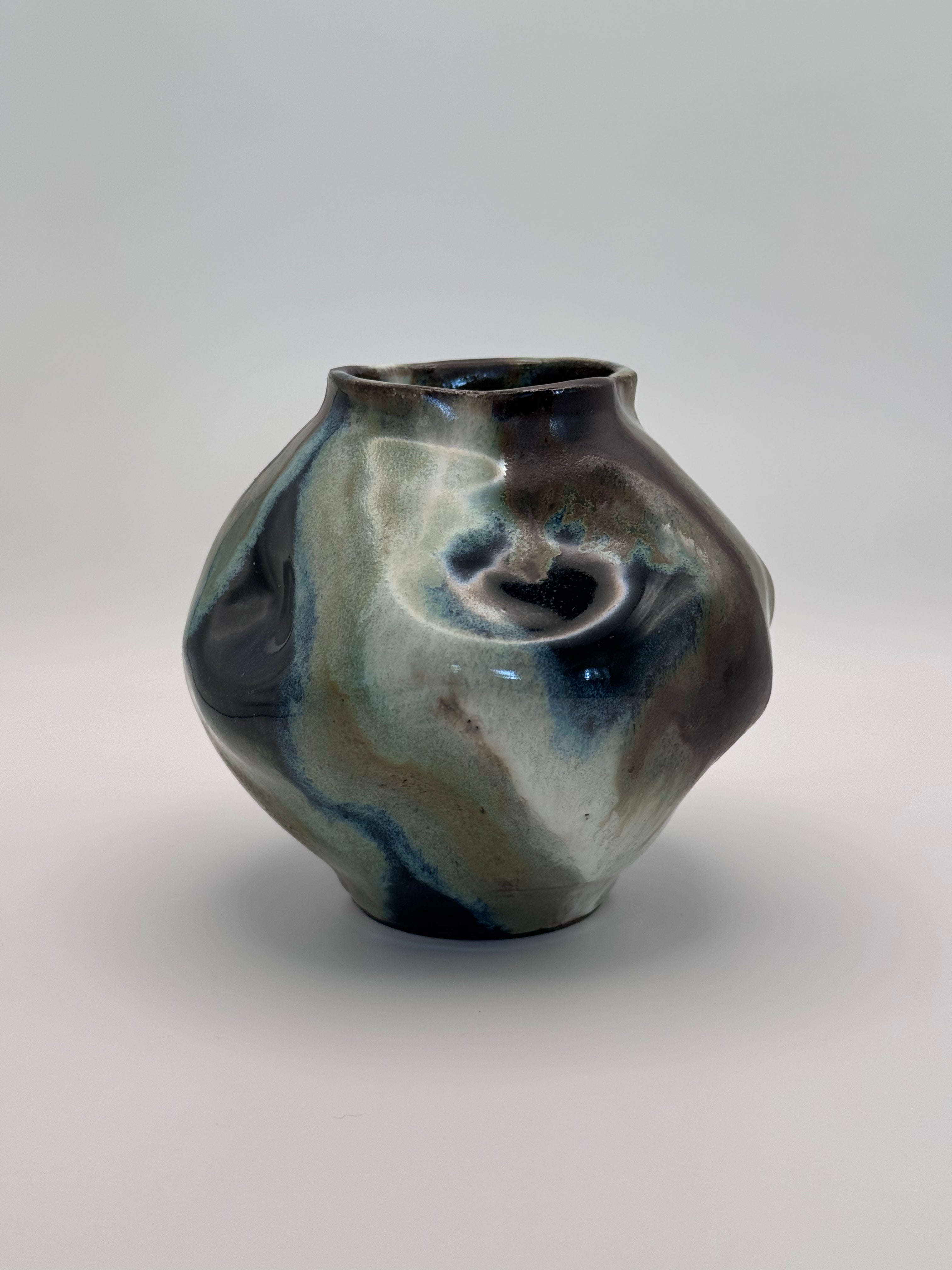 Hand-shaped ceramic vase with softly undulating walls and a wide mouth, marbled dark brown, white, green celadon, and light blue glaze.