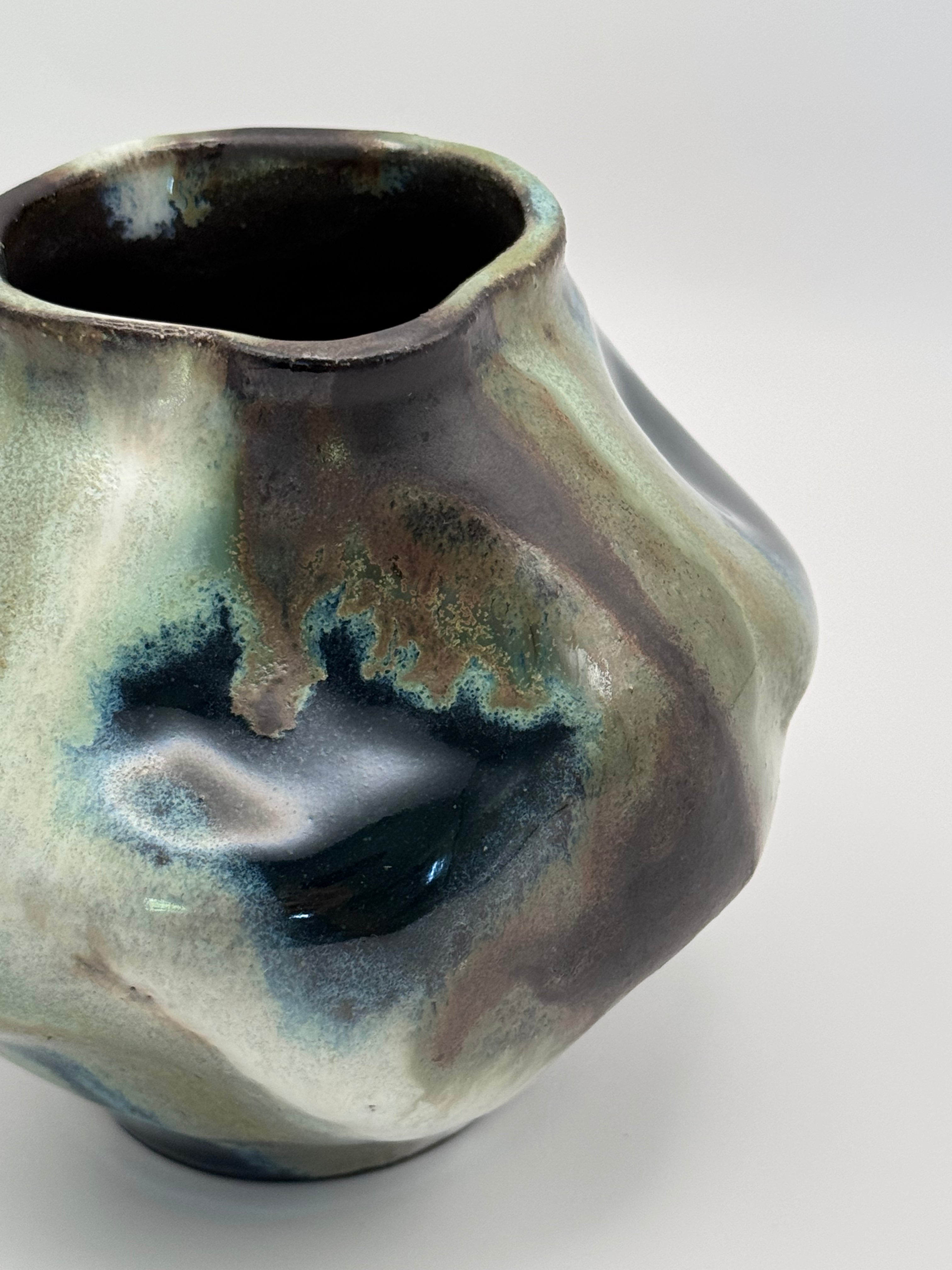 Side View of Hand-shaped ceramic vase with softly undulating walls and a wide mouth, marbled dark brown, white, green celadon, and light blue glaze.