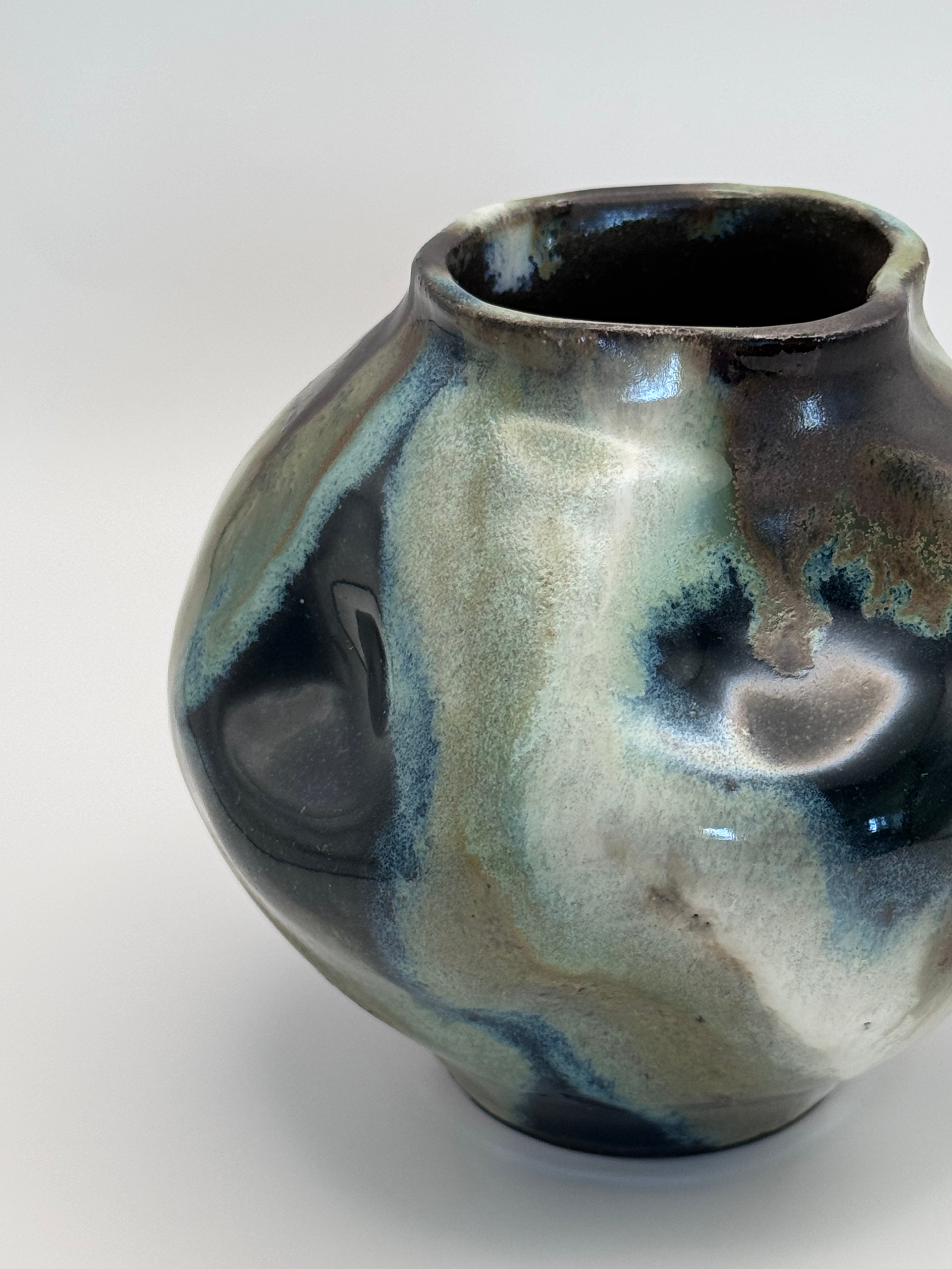 Close up view of Hand-shaped ceramic vase with softly undulating walls and a wide mouth, marbled dark brown, white, green celadon, and light blue glaze.
