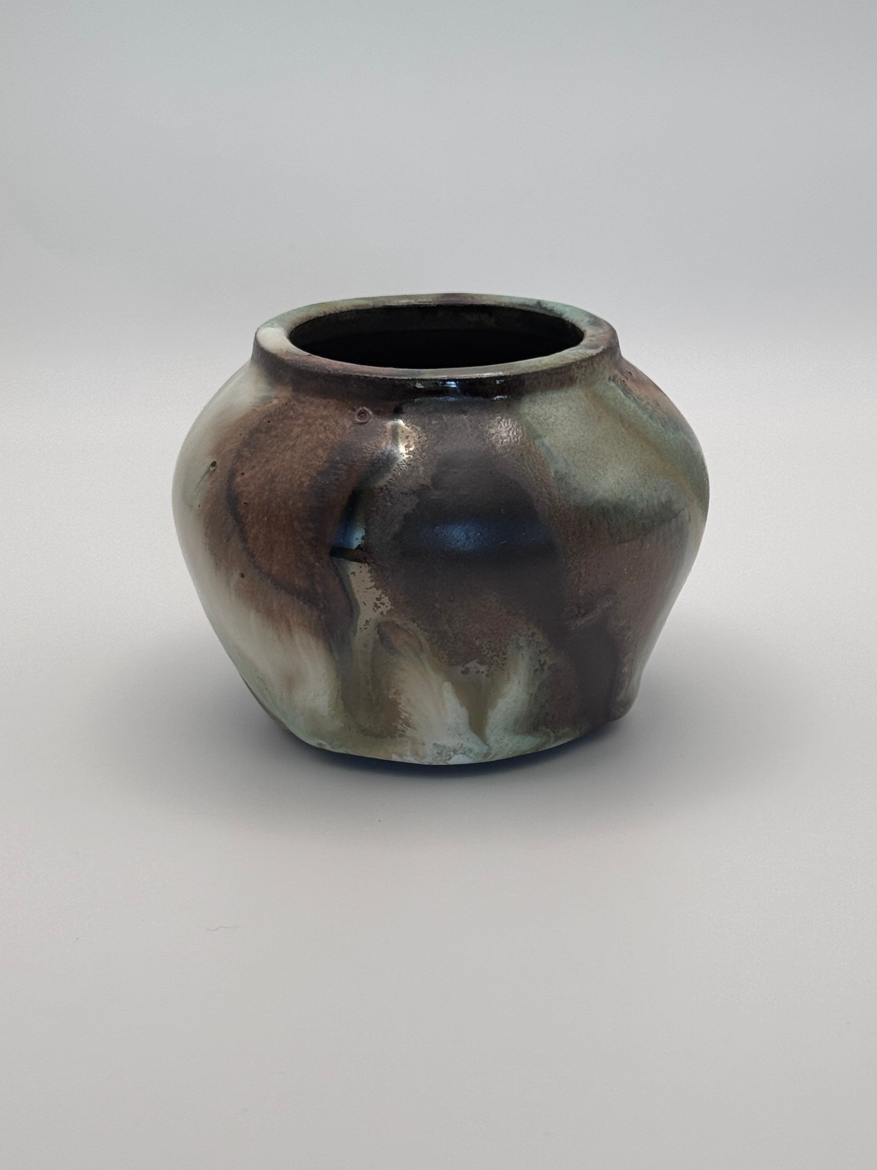 Small ceramic bud vase with rounded shoulders, marbled dark brown, white, and green celadon glaze with metallic crystalline accents. View 3 of 4