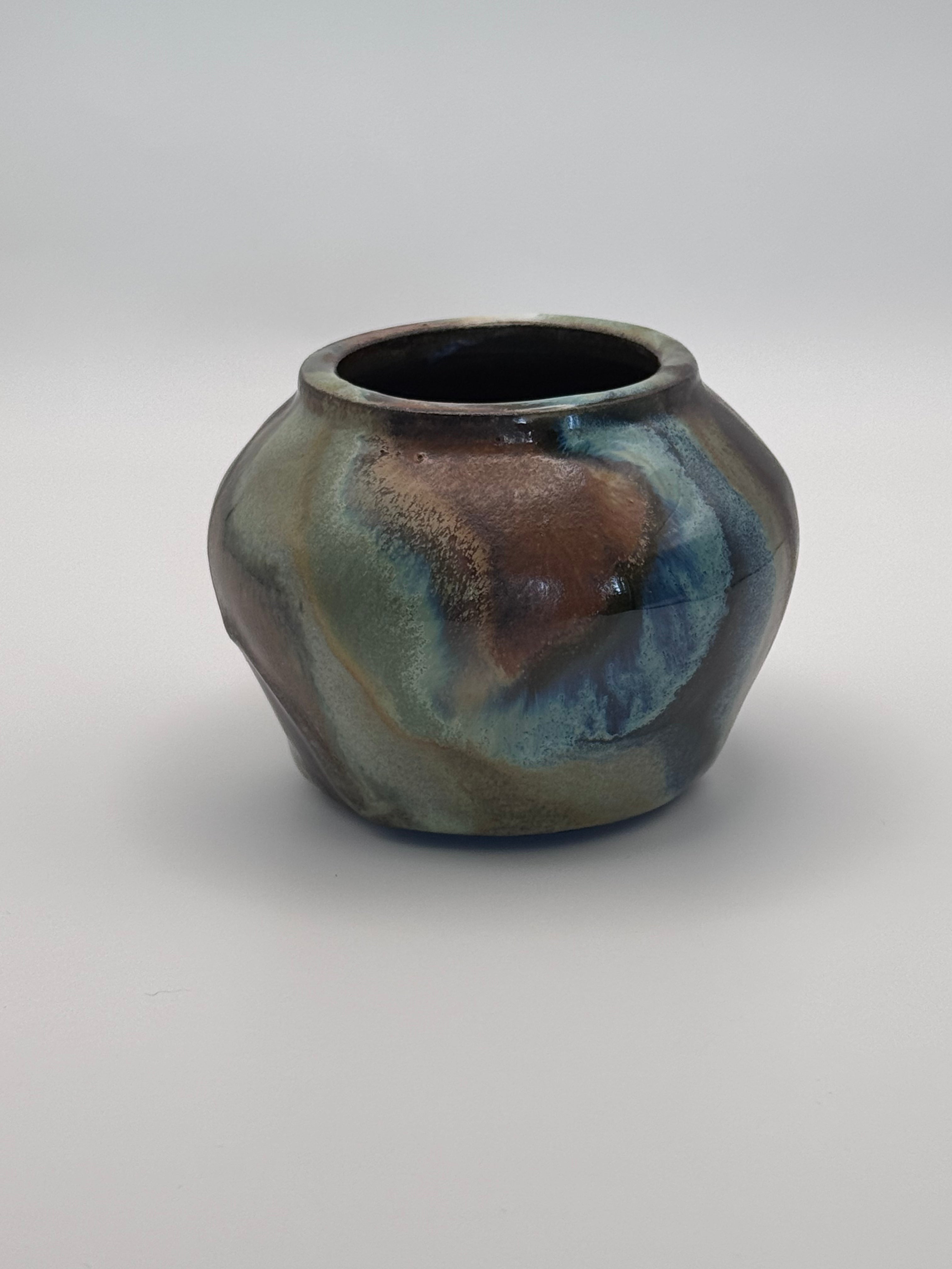 Small ceramic bud vase with rounded shoulders, marbled dark brown, white, and green celadon glaze with metallic crystalline accents. View 2 of 4