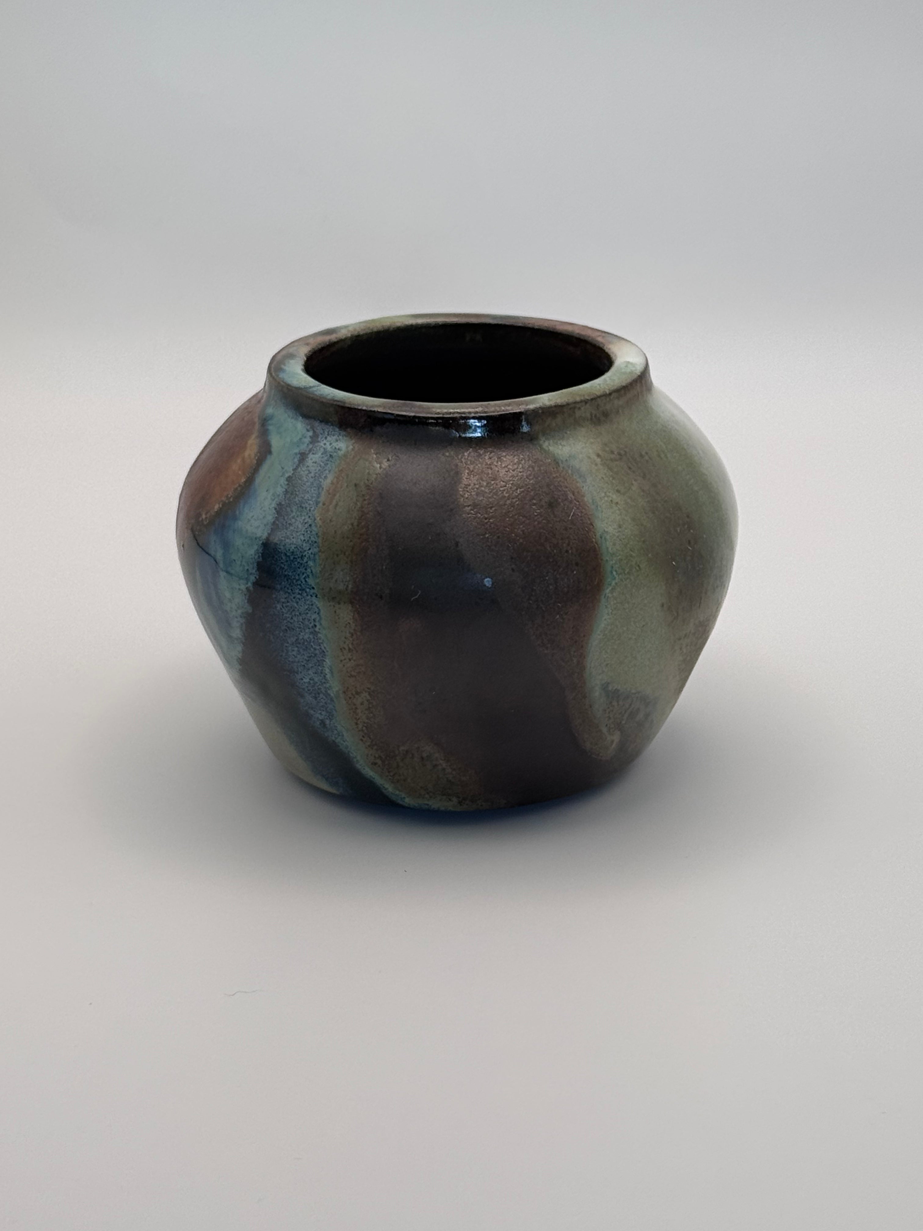 Small ceramic bud vase with rounded shoulders, marbled dark brown, white, and green celadon glaze with metallic crystalline accents. View 4 of 4