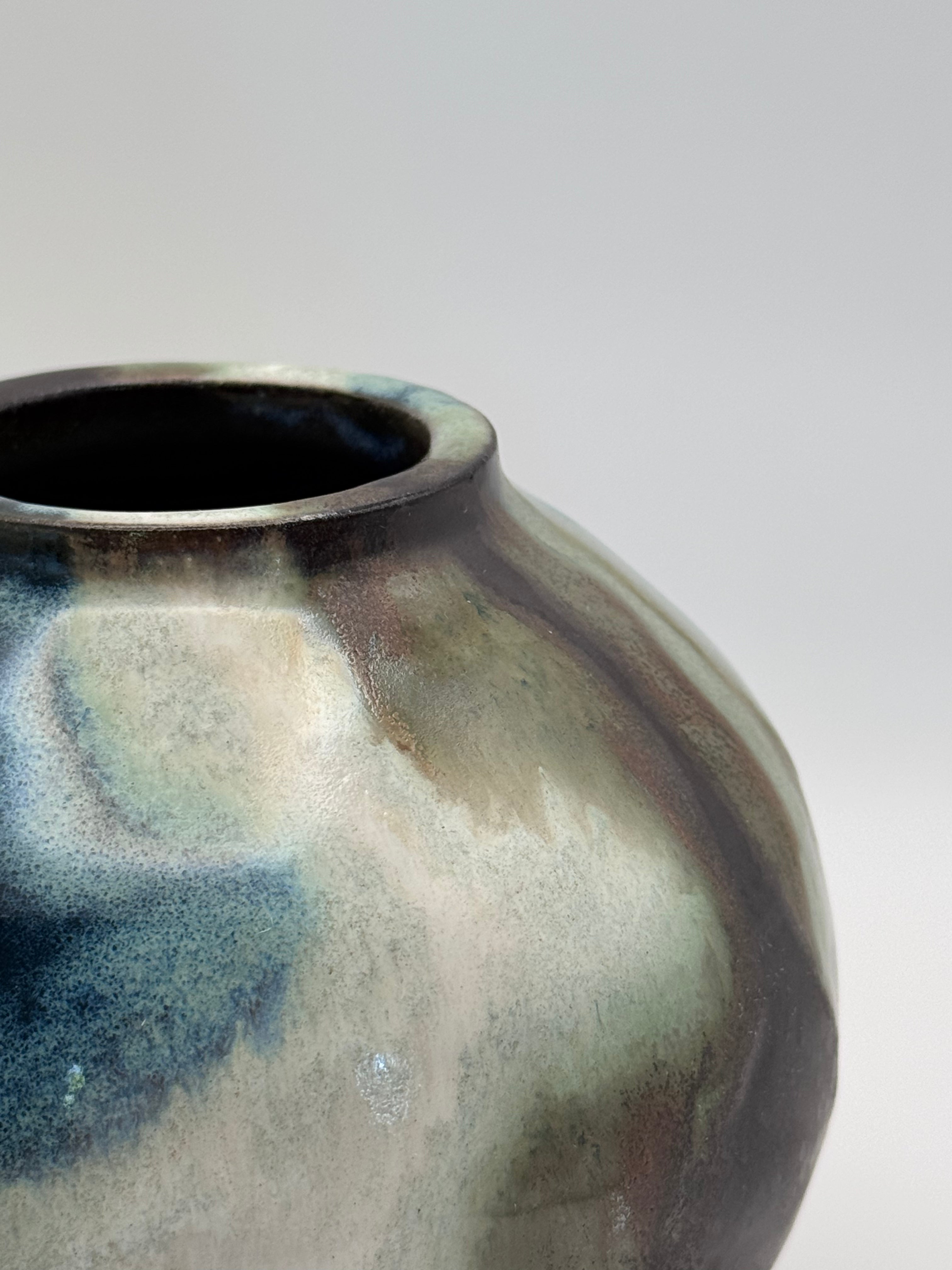 Close up view of rim of Round ceramic vase with a narrow mouth, marbled dark brown, white, green celadon, and light blue glaze.