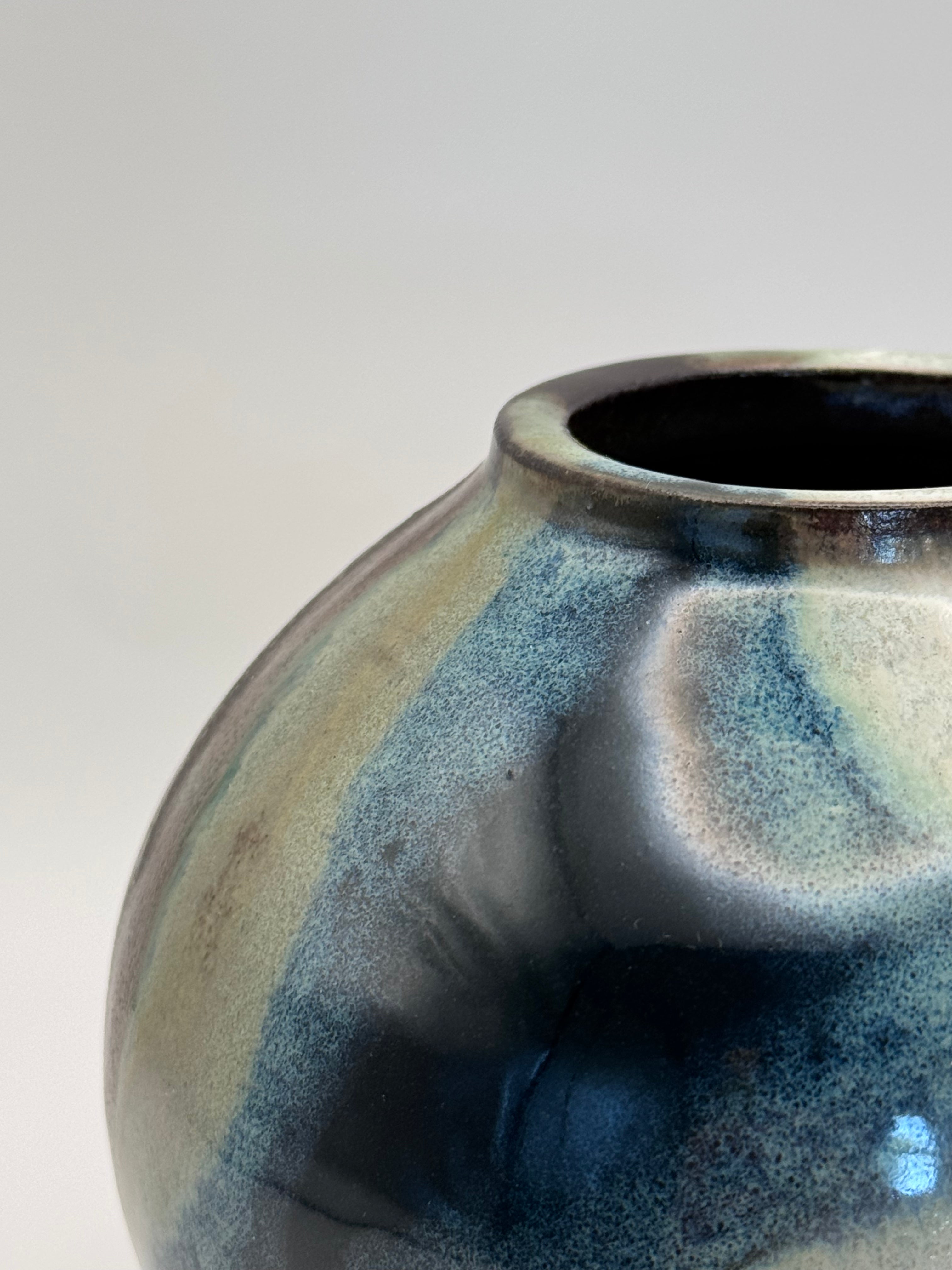 Close up of rim of Round ceramic vase with a narrow mouth, marbled dark brown, white, green celadon, and light blue glaze.