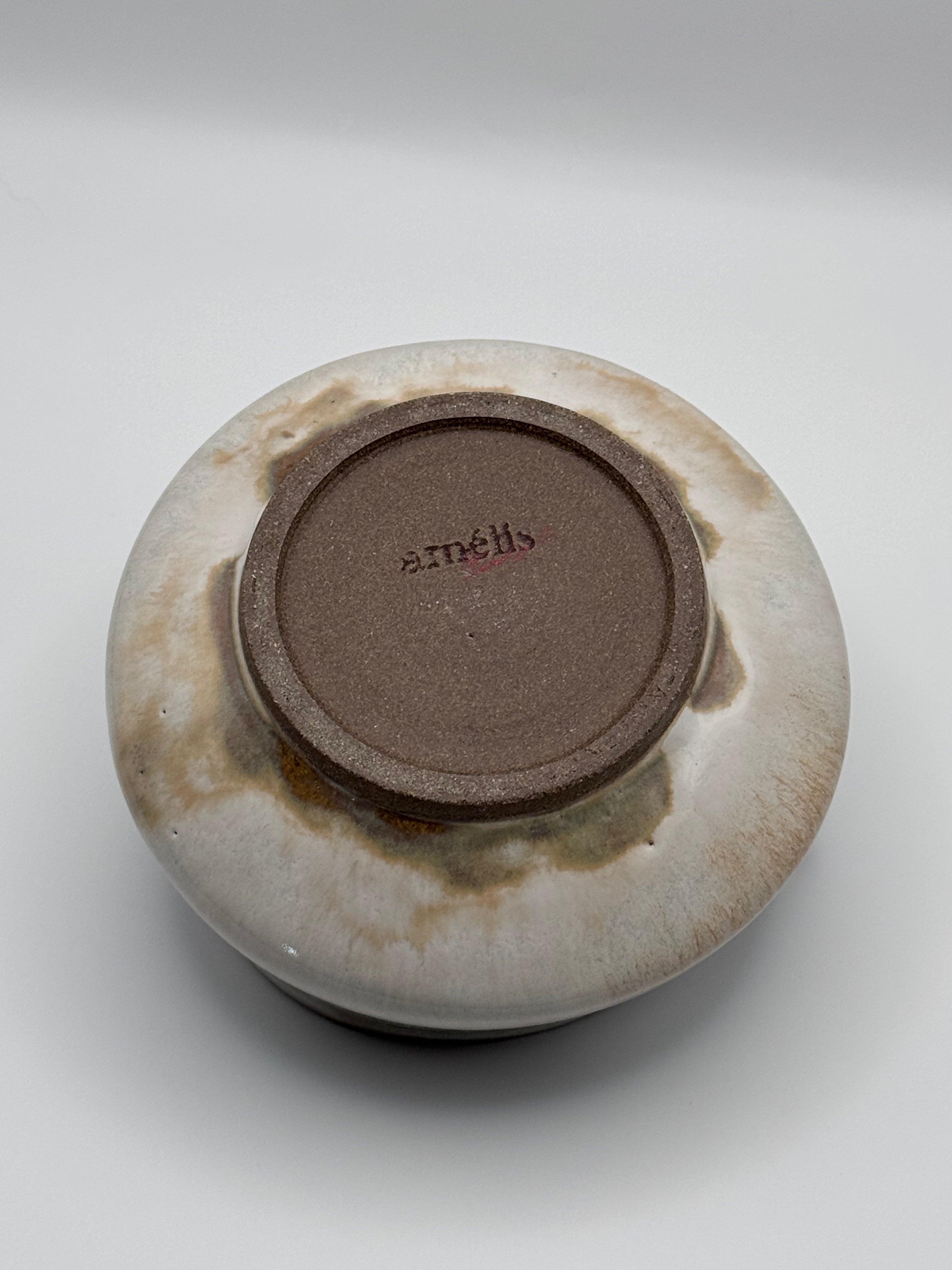 A ceramic bowl shown from the bottom, featuring a glossy brown center base with the brand name 'ST. MATHES' in red and a glazed exterior with beige, cream, and brown mottled patterns, set against a neutral gray background.
