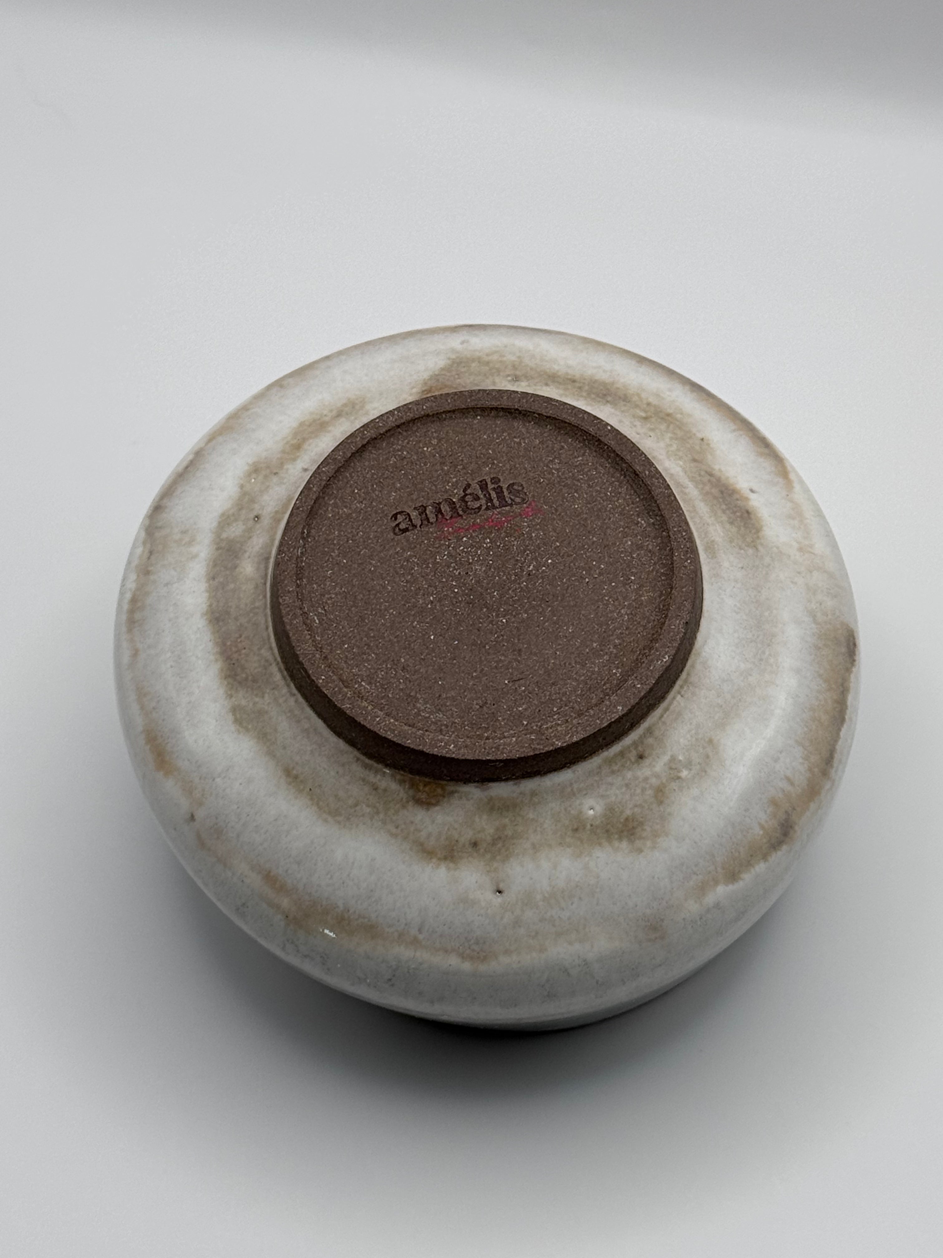 A round ceramic dish or bowl shown from the bottom, featuring a textured brown center with the brand name 'anélis' and a glossy off-white to light gray glazed exterior with subtle brown mottling.